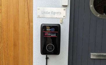 EV Charger installed by PM Electrical. Black charger on white wall of house.