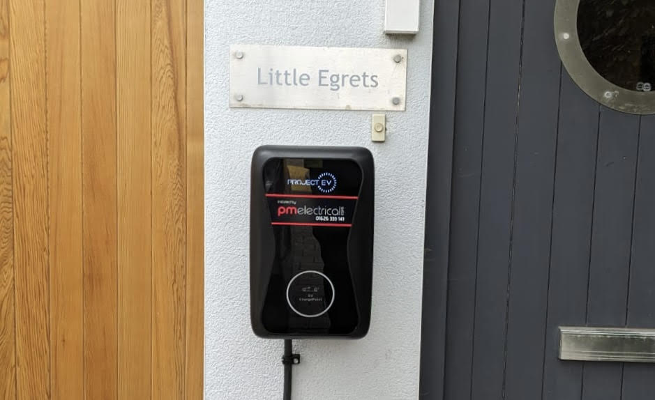 EV Charger installed by PM Electrical. Black charger on white wall of house. 